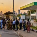Commuters queue at a bus stop beside a CNG refuelling station in a Nigerian city at sunset (AI-generated illustration)